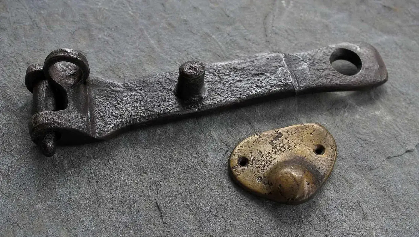 A wrought-iron gate latch and hinge on a weathered timber gate, close up