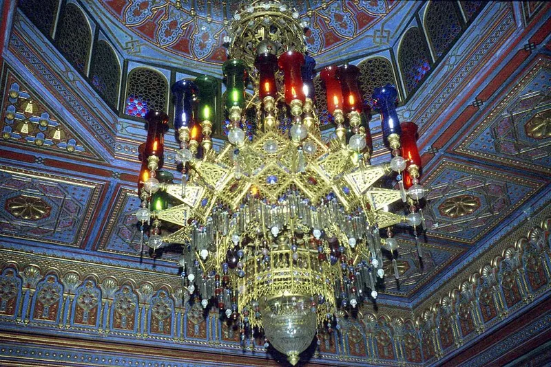 A chandelier of coloured glass seen from directly beneath, against a painted ceiling